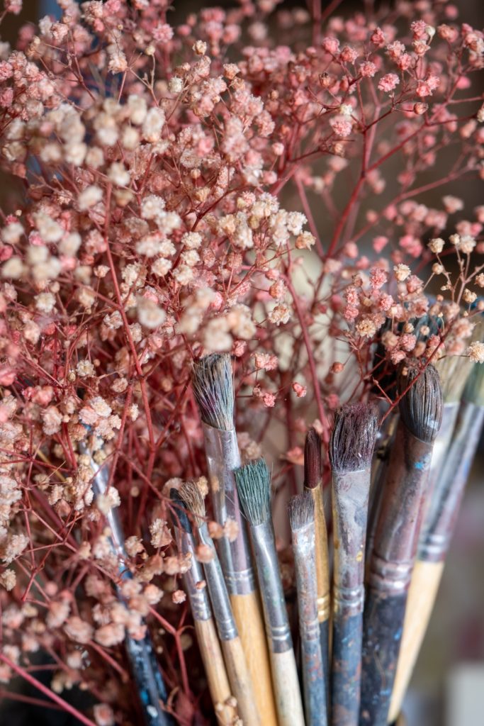 Pintura de interiores: Transforma tus espacios con una nueva paleta de colores y crea un ambiente acogedor y atractivo en tu hogar u oficina. 3  Conjunto de 10 pinceles utilizados en pintura de interiores junto a flores rojas con tallo rojo y flores blancas pequeñas