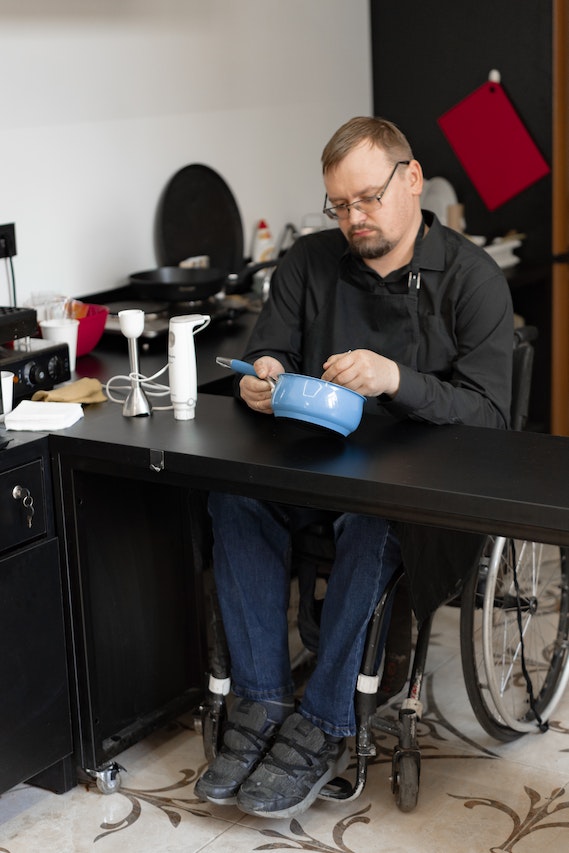 Reformas y adaptaciones para personas con discapacidad o movilidad reducida 6 Cocina adaptada para personas con movilidad reducida, hombre en silla de ruedas cocinando