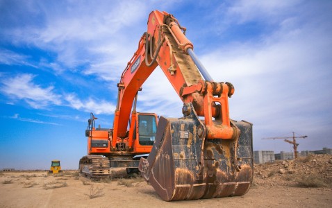 Vista de una máquina excavadora en pleno trabajo, nivelando el suelo bajo un cielo azul y nubes blancas. Máquina excavadora nivelando el suelo bajo un cielo azul con nubes blancas.