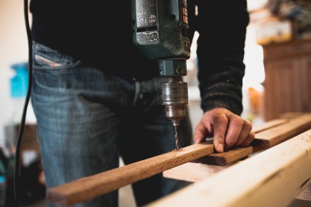 En esta imagen, un hábil operario utiliza una taladradora para realizar perforaciones en un listón de madera. Operario utilizando una taladradora en un listón de madera, precisión y habilidad en la carpintería