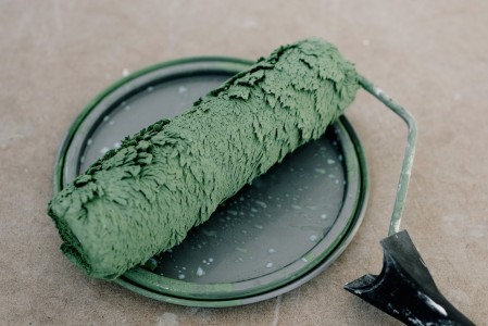 En esta imagen, podemos apreciar un rodillo de pintar descansando sobre un bote de pintura de color verde. El rodillo y la tapa del bote reflejan el tono de la pintura utilizada, indicando que se ha estado aplicando ese color en una renovación fresca y vibrante. Rodillo de pintar sobre un bote de pintura verde