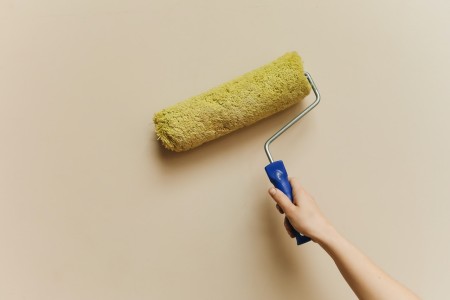En esta imagen, un hábil pintor se encuentra aplicando una capa de pintura en una pared interior de tono salmón claro. El rodillo se desliza suavemente sobre la superficie, transformando el ambiente con un toque vibrante y cálido. Pintor aplicando pintura en una pared interior de color salmón claro