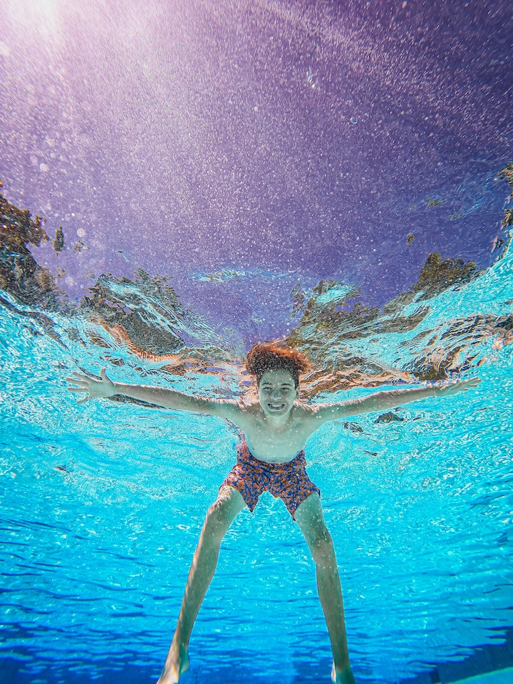 Renovación de una piscina 5 Imagen de un niño buceando en una piscina recién reformada, capturando su alegría mientras disfruta del agua bajo un hermoso atardecer en tonos morados y azules.
