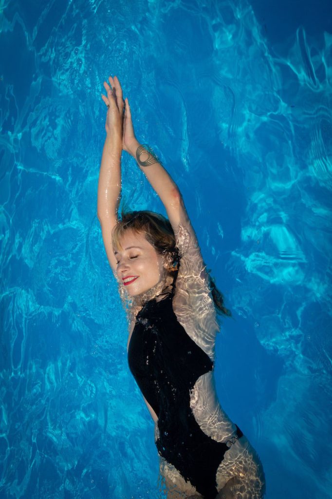 Renovación de una piscina 4 Imagen de una mujer joven disfrutando de una piscina recién reformada, con una sonrisa en su rostro mientras mira hacia el agua de espaldas.