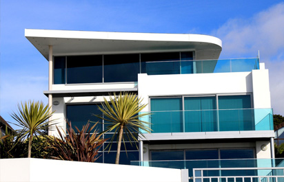 Servicios 10 Imagen de un edificio moderno de color blanco, con amplias cristaleras azuladas que reflejan el cielo azul y crean un efecto visual impactante.