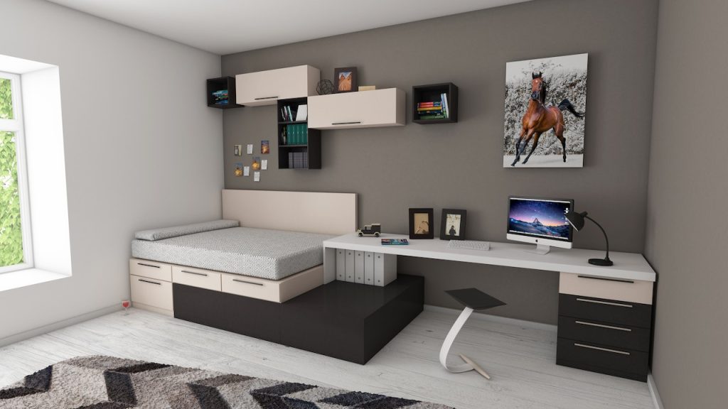 Montaje de muebles y elementos decorativos 2 Imagen de un dormitorio moderno con cama con cajones, escritorio amplio y estanterías en la pared en tonos crema, blanco y negro, con suelo de tarima blanca.
