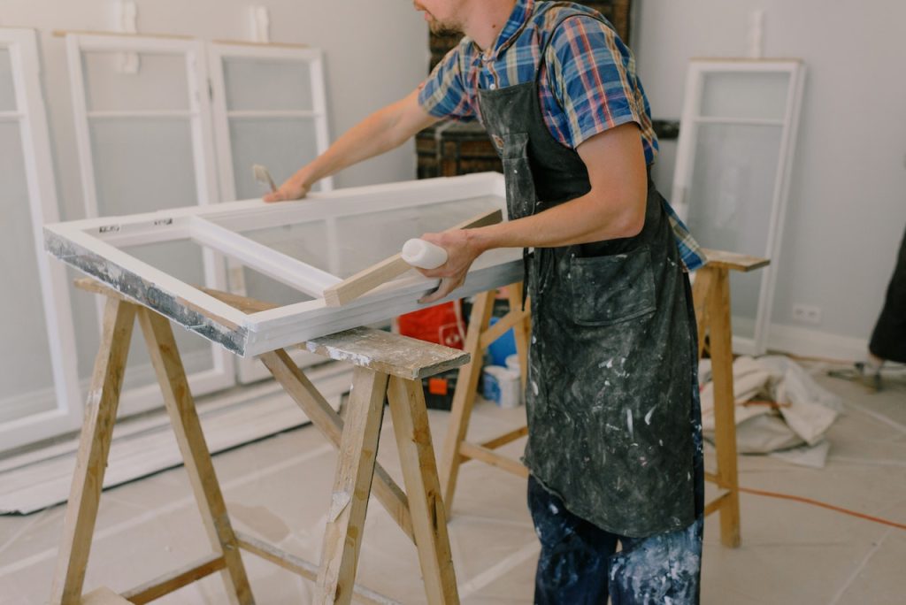 Instalación de carpintería (puertas, ventanas, armarios) 2 Operario manipulando una ventana en proceso de fabricación, apoyada en caballetes de madera.