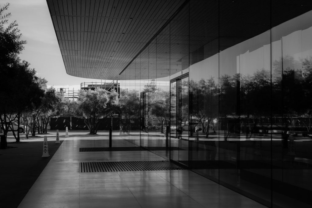 Colocación de revestimientos y pavimentos 2 Imagen en blanco y negro de un edificio de cristales con una puerta de cristal en primer plano, rodeada de un porche y un pavimento de estilo adoquín.